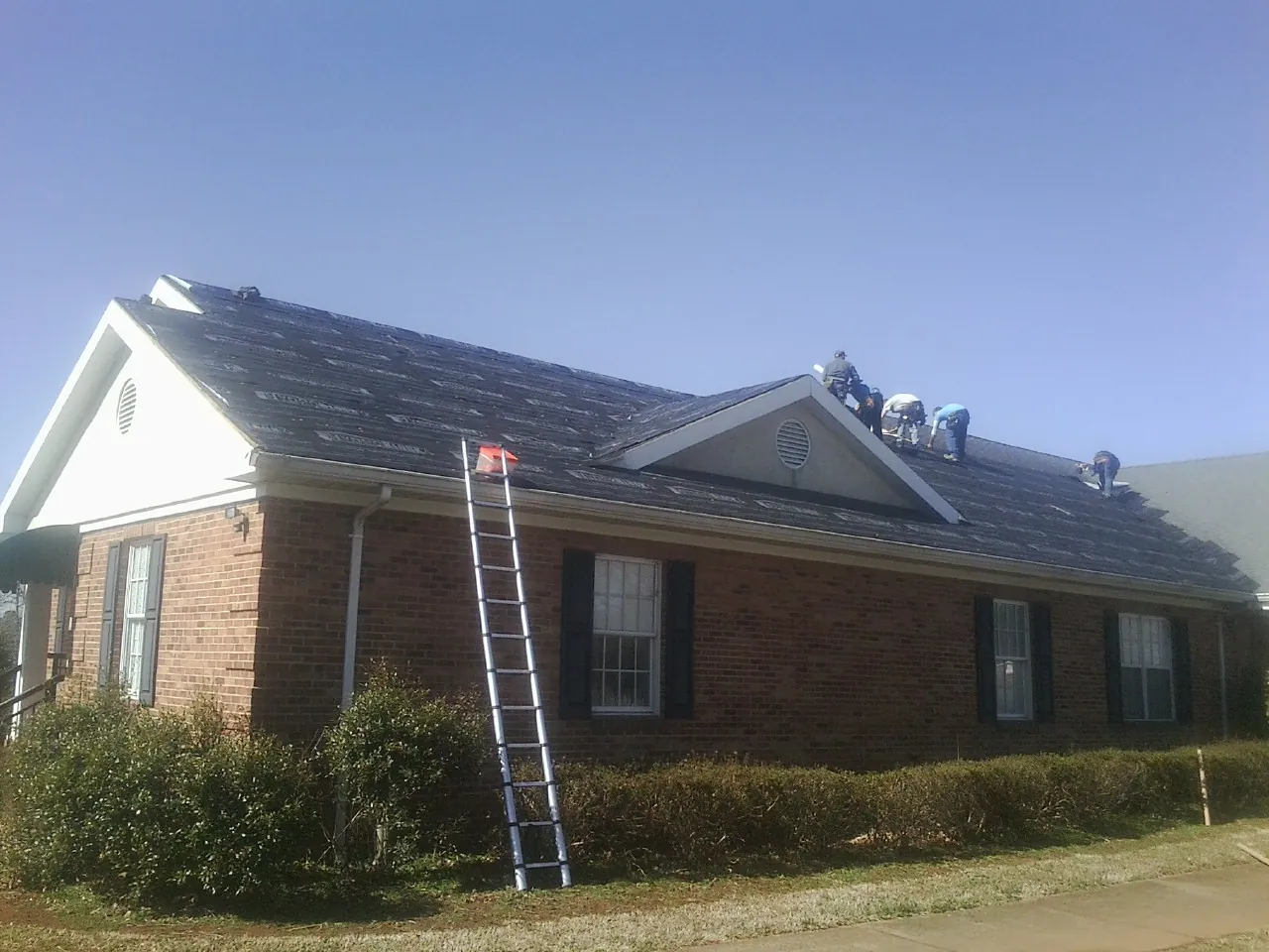 Crew tearing shingles off a brick ranch roof with a ladder set — Metal Roof Repair work by our crew in Davenport